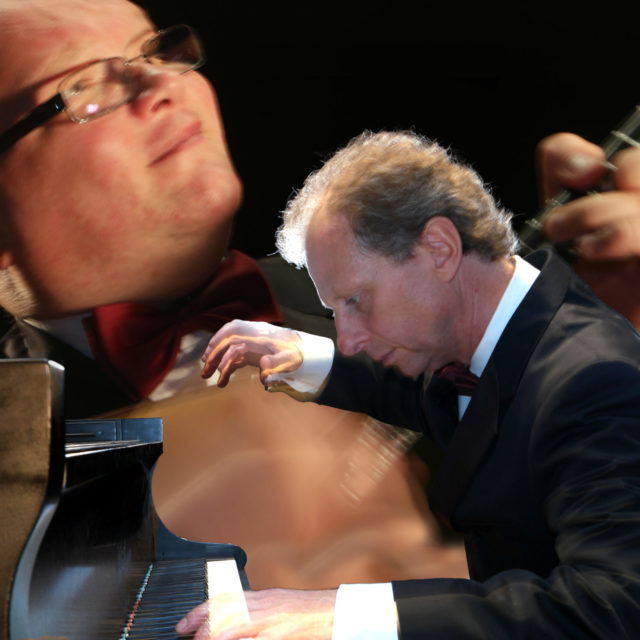 Mann spielt Klavier, trägt schwarzen Anzug und weiße Hemdmanschetten, konzentriert auf die Tasten