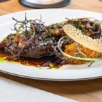 Ein Stück Fleisch, verziert mit Kräutern, auf einem weißen Teller