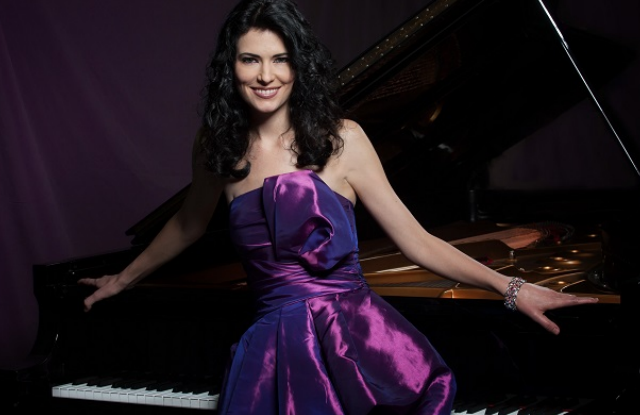 Frau in lila schimmernden ärmellosen Kleid steht mit ausgestreckten Armen an einem Klavier gelehnt.