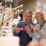 Ein warmgekleidetes Paar schaut sich Christbaumornamente in Form von Sternen in einem Geschäft an